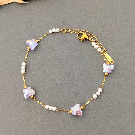 “Women’s delicate gold bracelet with purple butterfly crystals and pearl accents.”